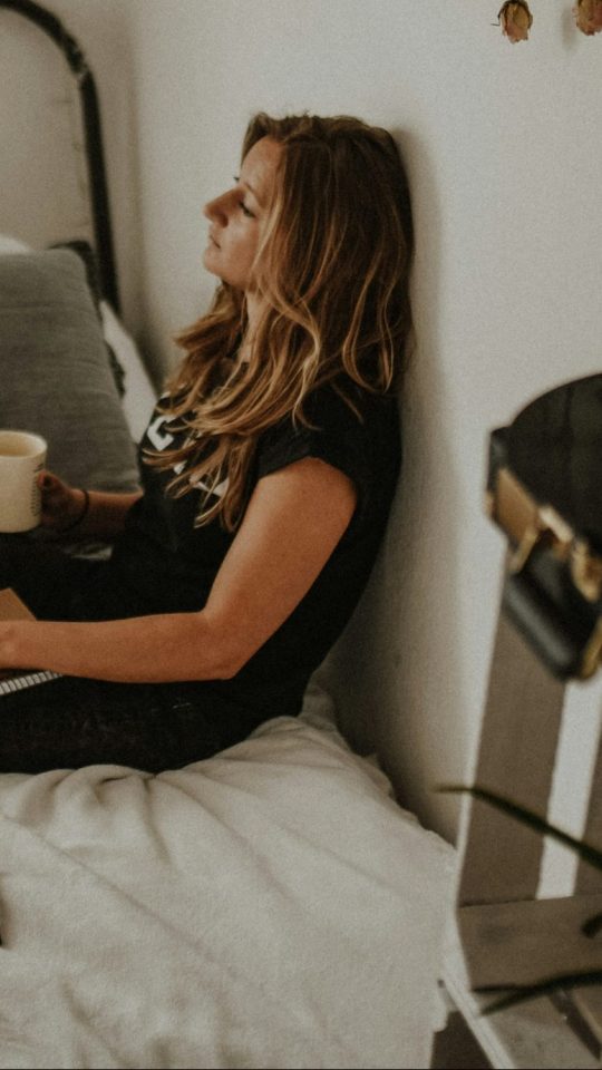 woman leaning on wall while sitting on bed
